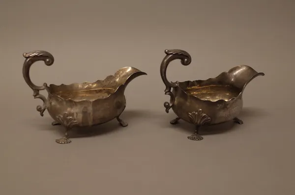 Two similar George III sauceboats, each with a scrolling handle, shaped rim and raised on three scallop feet, the hallmarks indistinct, combined weigh