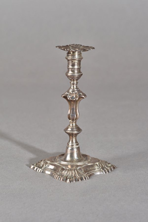 A George II silver taper stick, of cast form with a shaped stem, raised on a shaped square base, with scalloped corners, the detachable sconce unmarke