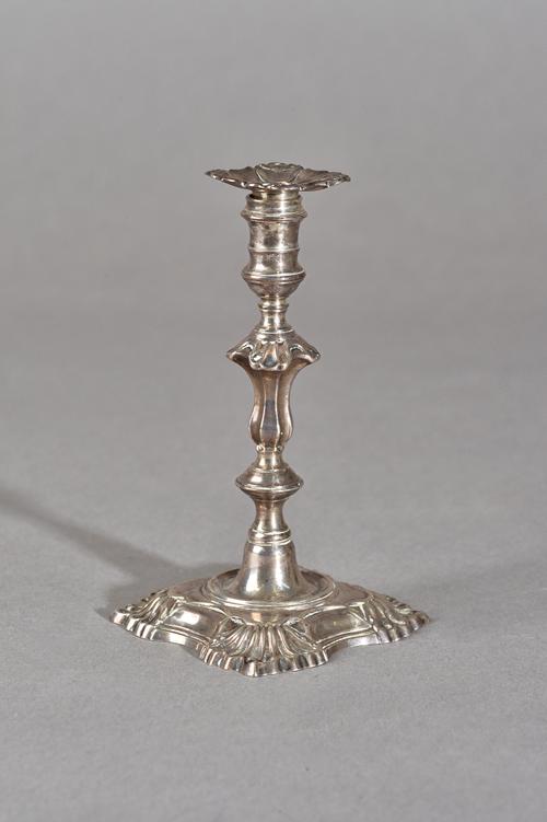 A George II silver taper stick, of cast form with a shaped stem, raised on a shaped square base, with scalloped corners, the detachable sconce unmarke