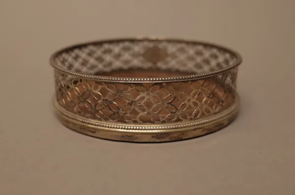 A silver mounted circular bottle coaster, with later pierced decoration within beaded rims and with a turned wooden base, diameter 12cm, London 1615