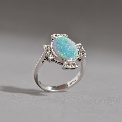 A platinum, opal doublet and diamond ring, in a cruciform design, mounted with the oval opal doublet to the centre, in a surround of two rows of three