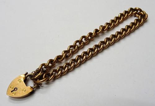 A 9ct gold solid curb link bracelet, on a 9ct gold heart shaped padlock clasp, fitted with a safety chain, weight 28.2 gms.
