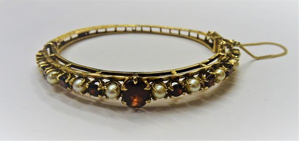 A 9ct gold, garnet and cultured pearl oval hinged bangle, claw set with the principal oval cut garnet, between alternating circular cut garnets and cu