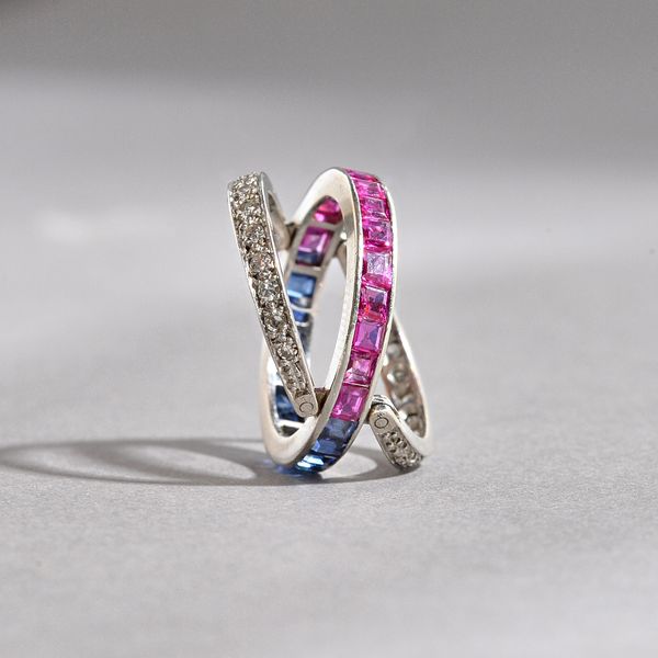 A diamond, ruby and sapphire set swingover and under eternity ring, the principal band mounted with a row of calibre cut rubies to one side and with a