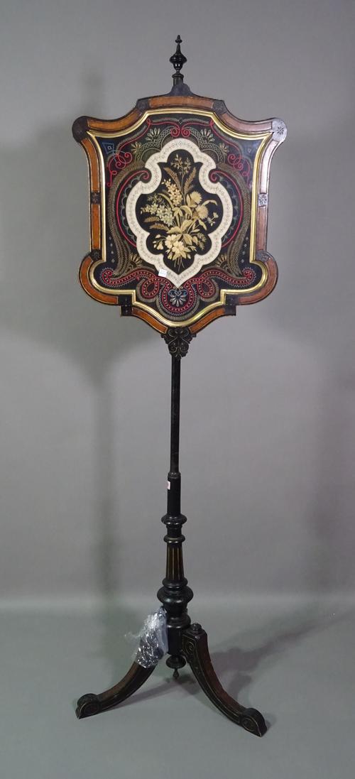 A 19th century Aesthetic movement pole screen with ebonised base, shaped supports and shield shaped embroidered screen, (a.f.).   C7