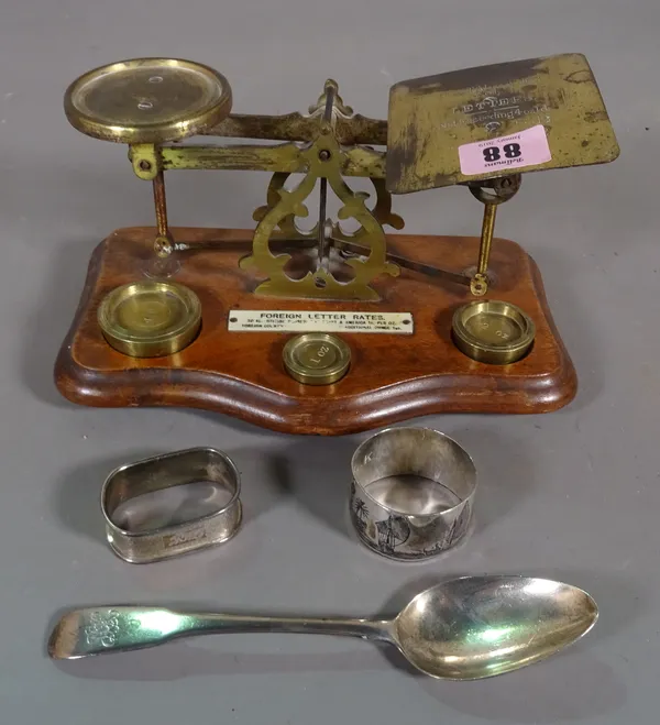A set of brass postage scales, a silver tea spoon and two napkin rings, (qty).  CAB