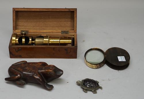A white metal novelty vesta cast as a tortoise and dated 1911, 6cm, a carved wooden 'frog' snuff box, 13cm, a horn magnifying lens and a brass student