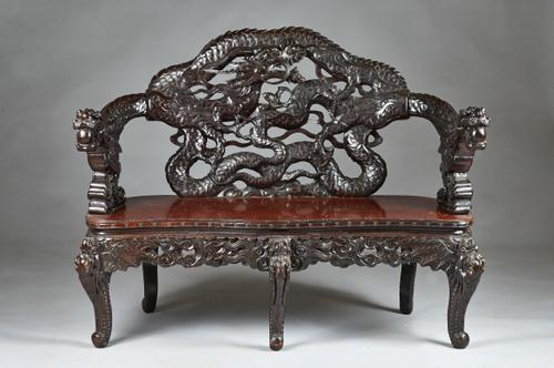 An early 20th century Chinese hardwood bench, the back carved with dragons chasing pearls over solid seat, 130cm wide x 102cm high. Illustrated