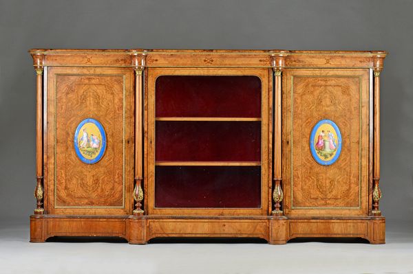 A Victorian gilt metal mounted figured walnut credenza, with glazed cupboard flanked by porcelain mounted cupboards divided by columns, 195cm wide x 1