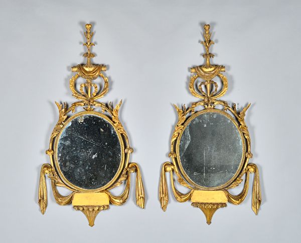 A pair of George III framed wall mirrors, each with ribbon and swag moulding about the oval mirror plate, 61cm wide x 115cm high. (2) Illustrated