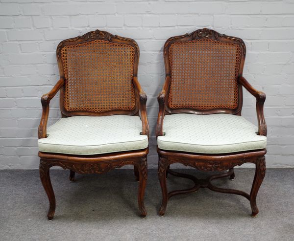 A pair of late 18th century French walnut cane back open armchairs with serpentine seat on cabriole supports, 64cm wide x 104cm high. (2)