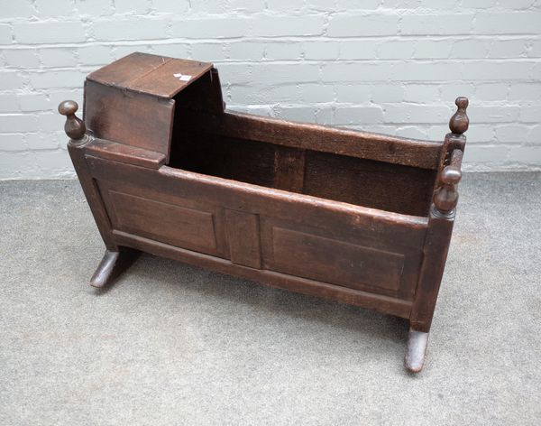 An 18th century oak rocking cradle, with integral hood and turned finials, 91cm wide x 60cm high.