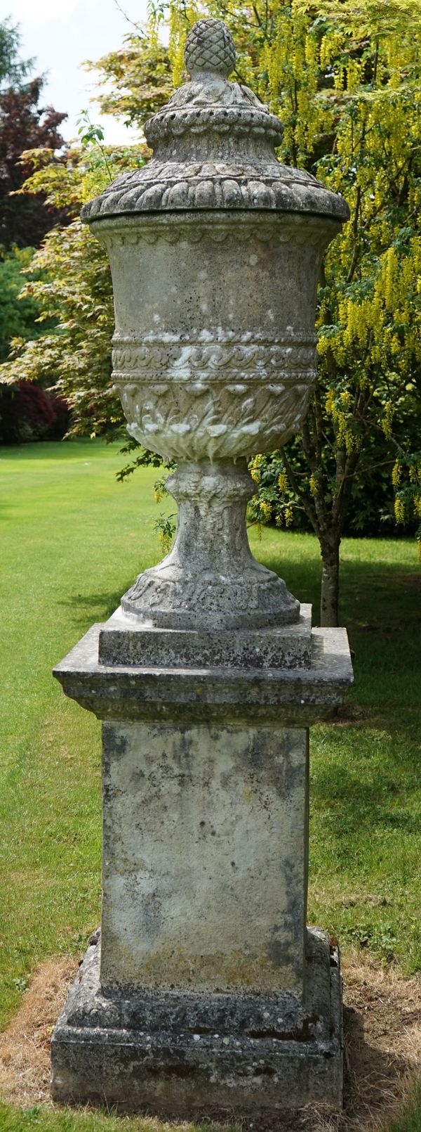 A pair of reconstituted stone urns, probably 20th century, on earlier square stone plinths, urns 130cms high, plinths 103cms high (weathered) (4)