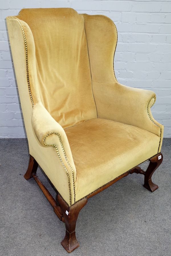 A George II style wingback armchair on square cabriole supports, united by turned stretcher, 90cm wide x 117cm high.