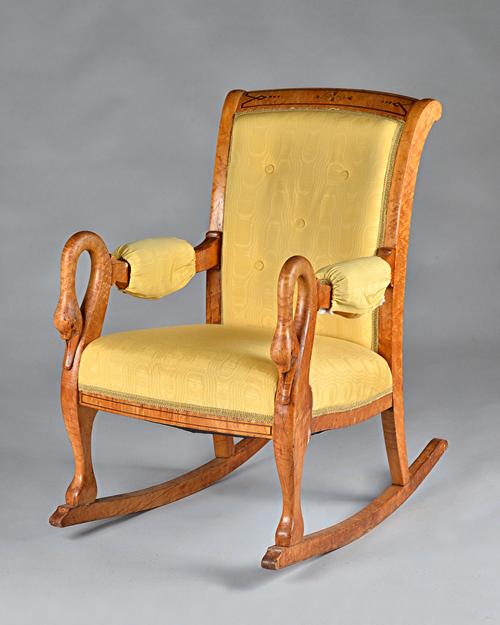 A Charles X field maple rocking chair, the arched back, armpads and bowed seat upholstered in part-buttoned yellow silk with swan arm-supports and scr