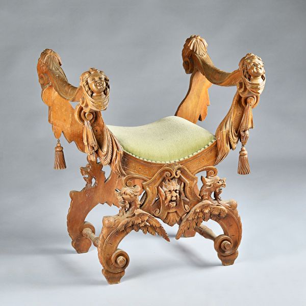 An Italian Renaissance style extensively carved X frame stool with cherub, Green Man and beast mask decoration, 70cm wide x 80cm high. Illustrated