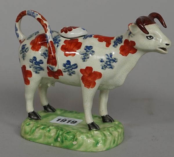 A pearlware cow creamer and cover, possibly Cambrian Pottery, Swansea, circa 1820-30, painted with iron-red and blue patches on a grassy mound base, (