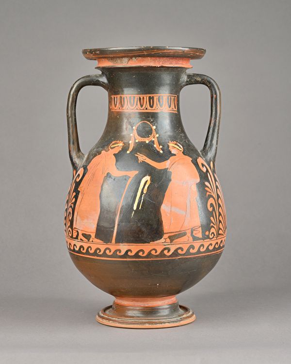 An Apulian red figure Pelike decorated with a nude winged Eros on a rocky out crop holding a fan and opposite a draped female leaing on a high basin a