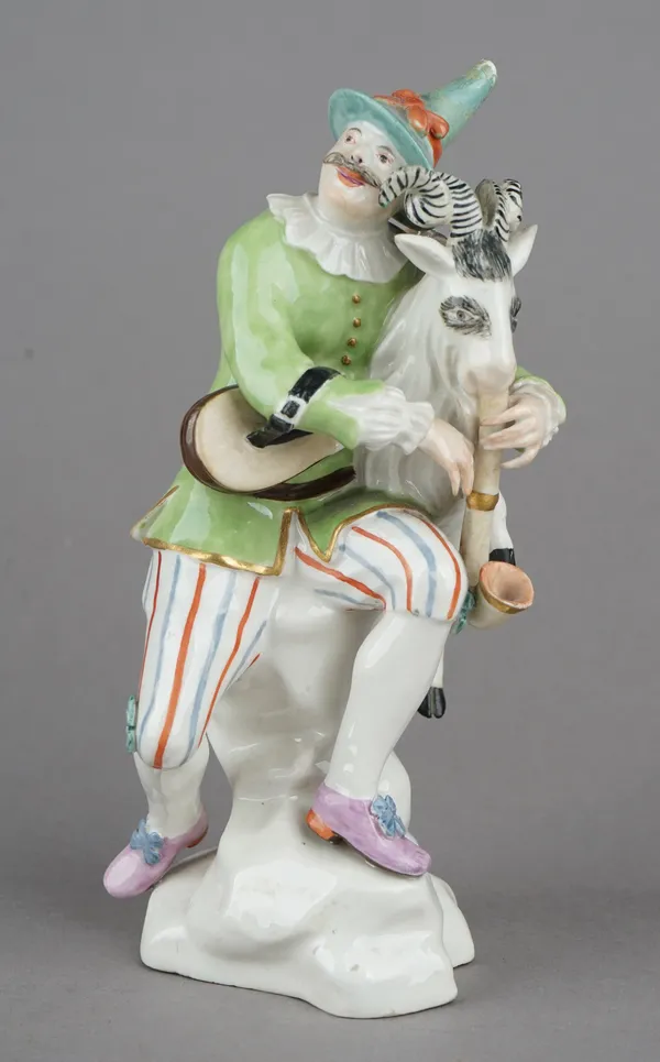 A rare Hochst porcelain figure of Harlequin playing  ram bagpipes, circa 1750-53, probably modelled by Johann Gottfried Becker, seated on a rocky moun