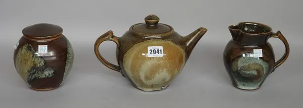 Clare Sutcliffe (1943-2019), a tea pot, milk jug and sugar jar, with shino dipped over ash and tenmoku glaze, makers marks, 16cm high, (3).