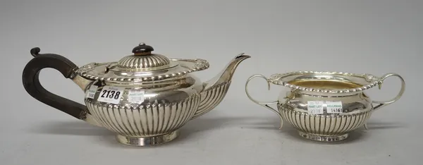 A silver teapot, of compressed circular form, with fluted decoration, black fittings and raised on a circular foot, together with a matching twin hand