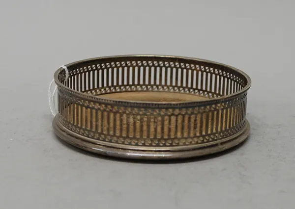 A silver mounted bottle coaster, decorated with a pierced gallery within a beaded rim and with a turned wooden base, diameter 12.5cm, London 1978.