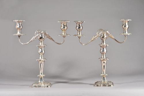 A pair of silver three light table candelabra, each with scrolling fluted arms and on a shaped square base, with foliate and floral cast borders, with