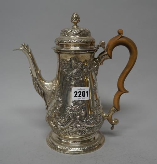 A late George II silver coffee pot, of baluster form, with floral, foliate and scroll embossed later decoration, crest engraved, the hinged lid with a