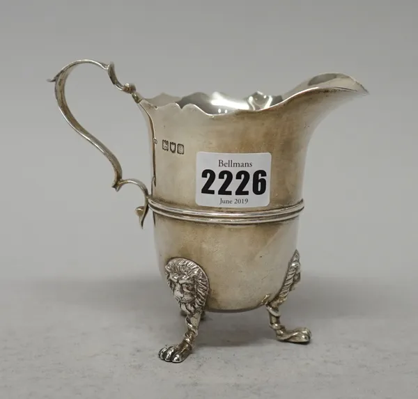 An Edwardian silver cream jug, with double scroll handle and wavy rim, raised on three lion mask feet, London 1902.