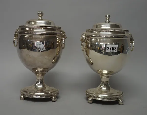 A pair of silver plate vase and covers in the Regency Style, each of ovoid form with twin lion mask and half ring handles upon four ball feet 28cms hi