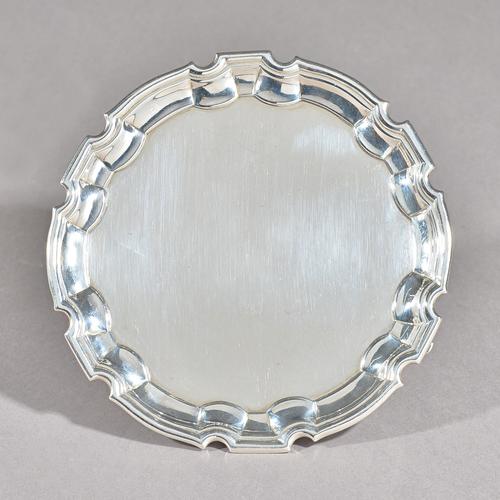 A George II silver card tray, of shaped circular form, having a pie-crust border and raised on three scroll feet, the underside engraved with a family