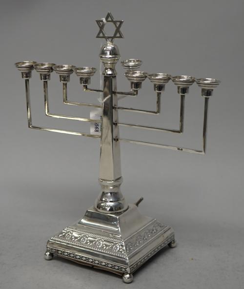 A silver musical menorah, mounted with a Star of David, raised on a stepped square base with beaded borders, (the base loaded), London 1951, height 25