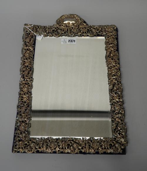 A late Victorian silver mounted strut backed mirror, of arched rectangular form, with pierced floral and scroll decoration, fitted with a bevelled gla