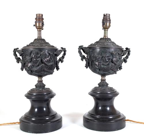 A pair of 19th century bronze twin handled urns, moulded with classical figures mounted on marble socles, later converted to lamps, 19cm wide x 42cm h