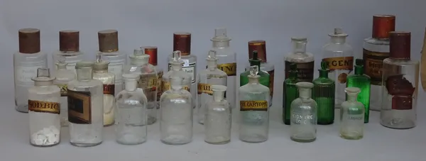 A quantity of glass apothecary jars, late 19th century and later, many with titled gilt labels, stopped and tin caps, the tallest 27cm high. (29)