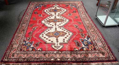 A Persian rug, red ground with triple pole medallion in ivory, boteh decoration, pale brown main border, 285cm x 210cm.