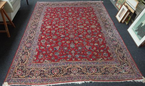 A Kashan carpet, Persian, the madder field with an allover floral sprays design, a dark indigo palmette floral spay and vine border, 360cm x 270cm .