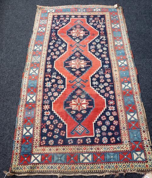 A Kazakh rug, Caucasian, the shaped madder field with three medallions, indigo surround with figures, animals and flowerheads, a box border, 228cm x 1