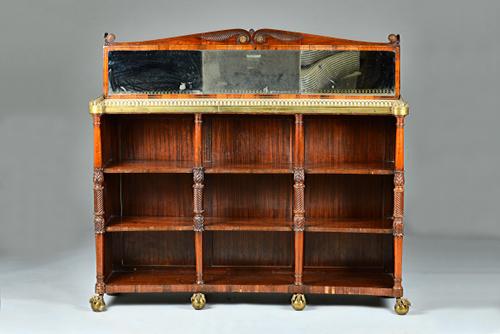 A Regency brass mounted concave bookcase, the marble top with mirror back over three open tiers divided by spiral turned columns on gilt metal claw an