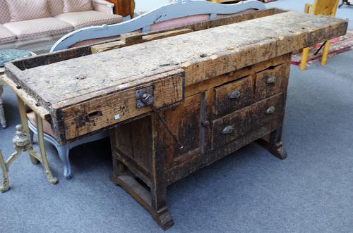 A 20th century beech and pine work bench, in distressed condition, the rectangular top with integral vice over three drawers and cupboard, 217cm wide