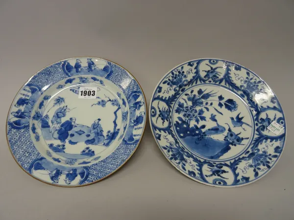 A Chinese blue and white plate, Kangxi, painted with three figures at leisure in a garden inside a diaper pattern border reserved with four figurative