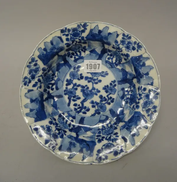 A Chinese blue and white moulded soup plate, Kangxi, painted in the centre with flowering prunus, beneath a panelled border enclosing flowers alternat