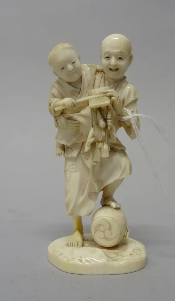 A Japanese ivory okimono, Meiji period, carved as a man carrying a child under his arm who holds a puppet, signed, 12cm. high.