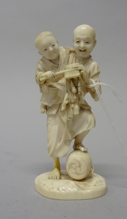 A Japanese ivory okimono, Meiji period, carved as a man carrying a child under his arm who holds a puppet, signed, 12cm. high.