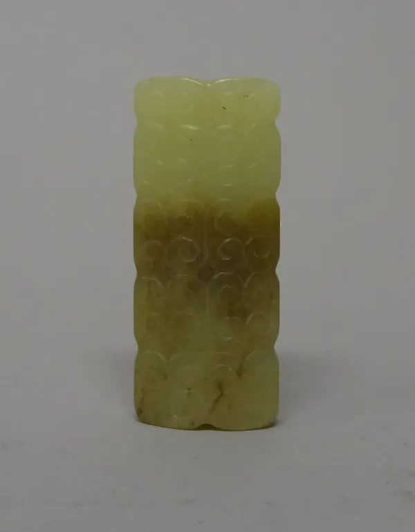 A Chinese jade rectangular bead, possibly Han dynasty, each side carved with scrolls, the stone of pale celadon and brown tone, 4.5cm. length.