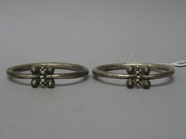 A pair of Persian silver armbands, 19th century, of rounded band form, terminating in four raised spiral circular elements around a central pin and ho