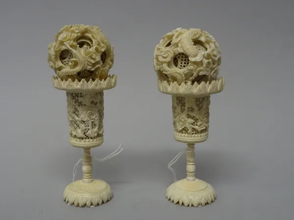 A near pair of Canton carved ivory puzzle balls on stands, late 19th/early 20th century, each ball carved on the outside with two sinuous dragons, the