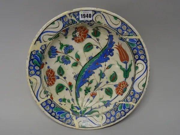 An Iznik pottery dish, early 17th century ,painted with tulips, roses and a saz leaf, the rim with a breaking wave design, (a.f), 31cm. diameter.