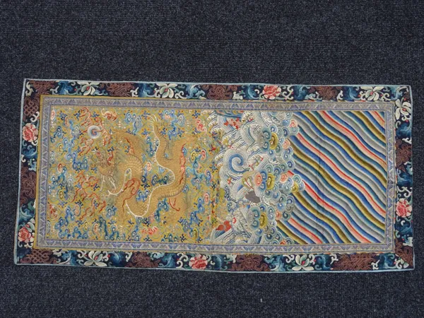 A Chinese embroidered silk rectangular panel, circa 1900, worked with a gold five-clawed dragon amongst clouds and auspicious symbols above breaking w