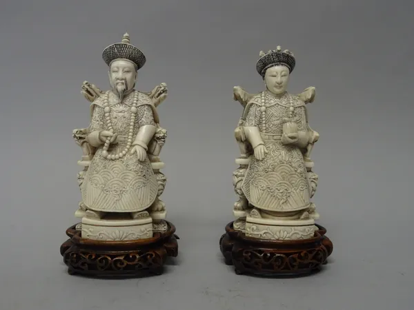 A pair of Chinese ivory figures of an Emperor and Empress, early 20th century, each carved seated on a throne, highlighted with black pigments, signed